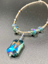 Load image into Gallery viewer, Make a bold statement with this shimmery aqua blue and gold tones glass beaded necklace. The large rectangular faceted shaped pendant creates a vivid contrast to the warm gold tones of the necklace, perfect for adding a rich pop of color to any Spring outfit. The draped design gives this piece an elegant, bohemian look. Measurements:    Necklace is 20” in length, 
