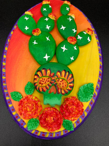 This handcrafted polymer clay wall art features a wood frame painted in a gradient from light yellow to dark red, creating a stunning sunset look. With a bright green skull cactus plant and bright yellow/red blooming flowers. Boasting vivid marigold blooms and a deep purple frame to make a bold contrast with the warm background hue. this piece is sure to make a statement.  Measurements: H 7