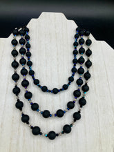 Load image into Gallery viewer, This statement piece features 3 long strands of flat matte black and dark blue glass beads, complemented by a floral metal beaded necklace. It gracefully drapes across the neck for a fierce, yet elegant look, making it perfect for cocktail chic attire, weddings, or minimalist styling.  Measurements:    Necklace is 16” in length - adjustable to 18&quot;
