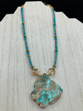 Load image into Gallery viewer, This vibrant and striking double strand necklace features a combination of glass beads in blue and green shades of turquoise, gold and champagne. The two delicate strands are accented with a gold-tone flower-shaped bead, a howlite stone chip dyed in turquoise, and shimmery, cross-faceted champagne-colored glass beads to complete the dramatic look.  Measurements:   Necklace is 17” and can be adjusted up to 19"

