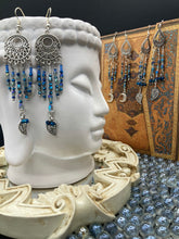Load image into Gallery viewer, These intricate moroccan blue Inspired large chandelier earrings boast five strands of blue and iridescent glass beads of various hues, including silver and gold. Additionally, two small dark blue glass beads with a silver leaf add a touch of dimension and motion. The perfect addition to any Fairy Princess or whimsical aesthetic.  Measurements: 4” in length
