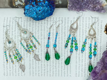 Load image into Gallery viewer, These large chandelier-style earrings feature blues, greens, and iridescent glass beads as well as a finely crafted silver plated leaf charm for added detail. Perfect for bohemian-inspired looks, these versatile earrings can elevate any wardrobe from whimsical hippie to boho chic.  Measurements: 3 1/4” in length
