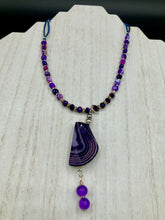 Load image into Gallery viewer, This double-stranded necklace is adorned with a large agate stone displaying a spectrum of purple shades, from light sheer to deep dark tones. The combination of purple agate and multi-colored glass beads makes this pendant a stunning addition to any summer look.  Measurements:  Necklace is 17” in length 

