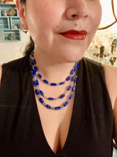 Load image into Gallery viewer, This vibrant royal blue and silver-tone necklace is adjustable and features an eye-catching three-strand design. The rectangular blue glass beads are predominant, complemented by a blend of lighter blue and silver beads for an intriguing multi-hued finish. By mixing shapes and tones, it creates a complex, dimensional look. The draped effect adds a fierce yet elegant pizzazz to any outfit. Perfect for the season of Spring, it will bring a splash of rich color to your wardrobe. 
