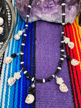 Load image into Gallery viewer, This sophisticated, yet dark-themed necklace utilizes small howlite skull beads along with black and white quartize floral beads to capture the iconic floral crown of Frida Kahlo. This Chingona, Cabrona, Latina Chicana, Goth, Vampire Goth, Dark Witchy Style jewelry can be used to inspire and to celebrate Dia de los Muertos. Equally suitable for dressy and casual outfits, the piece gives a unique edge to any look.
