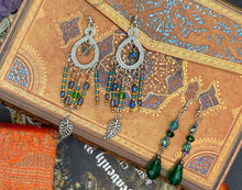 Load image into Gallery viewer, These large chandelier-style earrings feature blues, greens, and iridescent glass beads as well as a finely crafted silver plated leaf charm for added detail. Perfect for bohemian-inspired looks, these versatile earrings can elevate any wardrobe from whimsical hippie to boho chic.  Measurements: 3 1/4” in length
