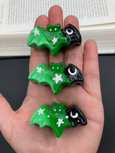 Cute and spooky magnet design to adorn your refrigerator, lockers, workstation, toolbox, or dishwasher. This hand-sculpted clay bat statuette boasts stunning ombre coloration, transitioning from black to dark green to light green to recreate the breathtaking look of a starry night sky.  H 1” x W 2” x D 1/2”