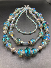Load image into Gallery viewer, This beautiful necklace features shimmery, rich aqua blue and silver tones glass beads. Its three strands consist primarily of faceted rondelle shaped beads, along with a variety of lighter blue and silver beads, resulting in a unique multicolored look. The perfect statement piece, this elegant necklace will drape beautifully across your neck, adding a vibrant hue to any Spring outfit.  Measurements:    Necklace is 18” in length
