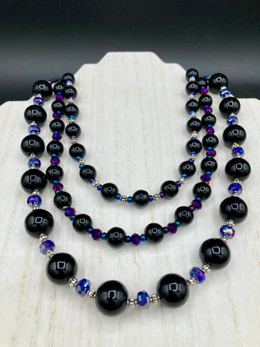 This Bohemian style necklace is composed of three strands of shimmery large black and dark purple glass beads, along with floral metal beads. The elegant drape creates a bold and fierce look that is ideal for a variety of occasions, such as cocktail chic attire and weddings. It is a perfect minimalist accessory.  Measurements:  Necklace is 16” in length - adjustable to 18
