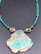 Load image into Gallery viewer, This vibrant and striking double strand necklace features a combination of glass beads in blue and green shades of turquoise, gold and champagne. The two delicate strands are accented with a gold-tone flower-shaped bead, a howlite stone chip dyed in turquoise, and shimmery, cross-faceted champagne-colored glass beads to complete the dramatic look.  Measurements:   Necklace is 17” and can be adjusted up to 19"
