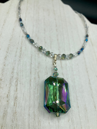 This gorgeous, Bohemian-style necklace features a shimmery aqua blue and gold-toned glass beaded design, with a large, faceted rectangular pendant adding dramatic flair. The vibrant and eye-catching colors make it the perfect way to add a pop of color to any ensemble and the draping style will give you a look that is both bold and elegant.  Measurements:    Necklace is 17” - adjustable to 18