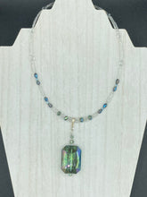 Load image into Gallery viewer, This gorgeous, Bohemian-style necklace features a shimmery aqua blue and gold-toned glass beaded design, with a large, faceted rectangular pendant adding dramatic flair. The vibrant and eye-catching colors make it the perfect way to add a pop of color to any ensemble and the draping style will give you a look that is both bold and elegant.  Measurements:    Necklace is 17” - adjustable to 18&quot;, pendant is 2 1/4”
