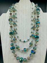 Load image into Gallery viewer, This beautiful necklace features shimmery, rich aqua blue and silver tones glass beads. Its three strands consist primarily of faceted rondelle shaped beads, along with a variety of lighter blue and silver beads, resulting in a unique multicolored look. The perfect statement piece, this elegant necklace will drape beautifully across your neck, adding a vibrant hue to any Spring outfit.  Measurements:    Necklace is 18” in length
