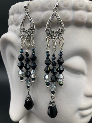This stylish three-strand black and silver glass beaded earring design presents a beautiful dancing effect, boasting a large black teardrop glass bead. A versatile accessory, it suits a variety of ensembles from cocktail chic to wedding fineries, and its minimalist aesthetic lends a modern charm.  Measurements: 3 3/4” in length