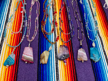 Load image into Gallery viewer, This exquisite necklace features a vibrant Sea Blue Agate Natural Stone Pendant and two strands of multi-colored glass beaded necklace. An adjustable collar-style strand contains small, light blue beads and lots of iridescent double-hole beads for shimmer and sparkle. The longer strand features larger blue glass beads interspersed with clear and silver beads for a sophisticated, draped look. It's finished with a set of dainty matching earrings for a complete look. Necklace is 14”adjustable up to 18"
