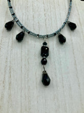 Load image into Gallery viewer, This adjustable collar-style necklace features silver and black glass beads in a combination of both teardrop and rectangular shapes, designed to create visual complexity and depth. The two strands are held together with two-hole silver and black beads, creating a stunningly bold and elegant draped collar that enhances any outfit.
