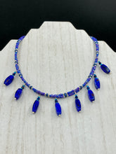 Load image into Gallery viewer, This Vibrant Royal Blue Glass Beaded Choker Necklace features two adjustable strands of deep blue beads with purple hues. The Bohemian style jewelry includes a mixture of rectangular-shaped blue, purple, and silver glass beads, which come together to create an eye-catching and elegant look. Perfect for any outfit, this draping necklace will add a vibrant and bold touch to your style.  Measurements:    Necklace is 14 3/4” in length, can be adjusted up to 16"
