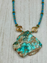 Load image into Gallery viewer, This vibrant and striking double strand necklace features a combination of glass beads in blue and green shades of turquoise, gold and champagne. The two delicate strands are accented with a gold-tone flower-shaped bead, a howlite stone chip dyed in turquoise, and shimmery, cross-faceted champagne-colored glass beads to complete the dramatic look.  Measurements:   Necklace is 17” and can be adjusted up to 19"
