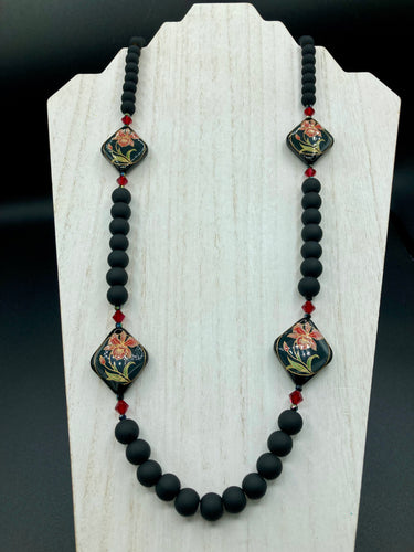 This statement necklace features elegant black matte glass beads with a smooth and velvety finish. Four ornamental ceramic beads with a traditional red, golden, and green pattern create a classic aura and luster-speckled dark red beads bring a striking final touch to the singular look.  This necklace is simple and elegant piece, very versatile look. Perfect cocktail chic attire, fancy wedding necklace, a minimalist look. Necklace: 32” in length 