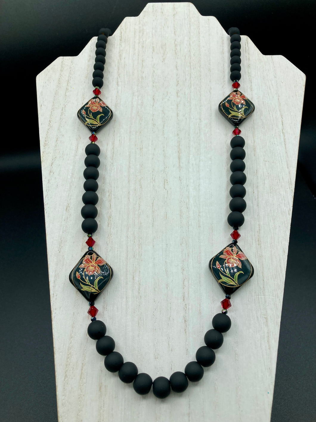 This statement necklace features elegant black matte glass beads with a smooth and velvety finish. Four ornamental ceramic beads with a traditional red, golden, and green pattern create a classic aura and luster-speckled dark red beads bring a striking final touch to the singular look.  This necklace is simple and elegant piece, very versatile look. Perfect cocktail chic attire, fancy wedding necklace, a minimalist look. Necklace: 32” in length 