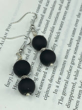 Load image into Gallery viewer, These flat matte black glass bead earrings are perfect for creating a cocktail chic ensemble. With a round shape and silver plated floral bead, this timeless piece is ideal for special occasions such as weddings. Its minimalist look exudes effortless elegance. Measurements: 1 1/4” in length
