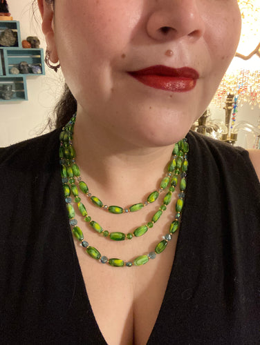 This adjustable glass beaded necklace features a combination of vivid green, blue, and gold hues and a mixture of shapes, creating an eye-catching spectrum of colors and a complex look. The rectangular green glass beads form the predominant part of the three-strand piece, which offers a bold and elegant fashion statement that is ideal for the Spring season.  Measurements:    Necklace is 17” in length, can be adjusted up to 19