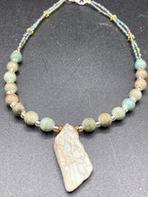 Load image into Gallery viewer, This exquisite necklace showcases earthy tones of mossy green ceramic beads, complemented by a gray toned howlite stone chip pendant. To add a sparkle, I interspersed gold-tone glass beads between each ceramic one. Two delicate strands feature small glass beads with hues of blue, gold, and purple. These are bridged by flower-shaped gold plated beads, which then unite with the round ceramic beads. This alluring earth-tone combination makes a stunning accessory. Necklace is 17” 
