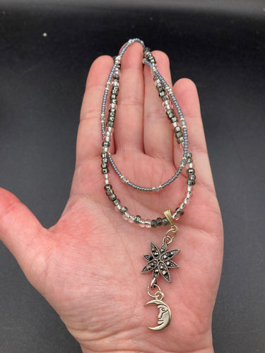 This Dainty Smiling Crescent Moon And Star Silver And Gray Choker Style Necklace features a variety of shimmering glass beads in light silver and gray tones. Varying in shape and size, these beads lend a unique and witchy celestial vibe to the necklace.  Measurements:  Necklace is 15 3/4”adjustable up to 18