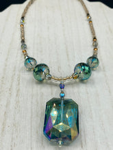 Load image into Gallery viewer, Make a bold statement with this shimmery aqua blue and gold tones glass beaded necklace. The large rectangular faceted shaped pendant creates a vivid contrast to the warm gold tones of the necklace, perfect for adding a rich pop of color to any Spring outfit. The draped design gives this piece an elegant, bohemian look. Measurements:    Necklace is 20” in length, 
