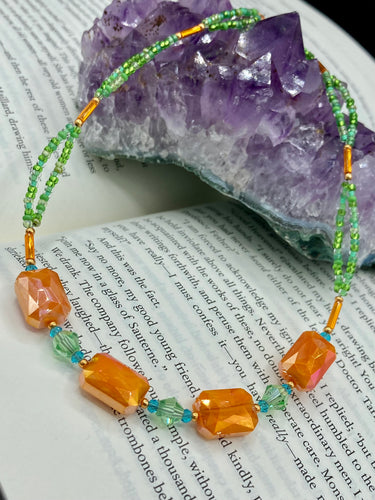 This unique, double-strand necklace consists of a blend of glass beads, including multi-green and rectangular, faceted orange glass beads, and is accented with gold and light blue elements. The vibrant combination is perfect for any summer look and will enhance any outfit.  Measurements:  Necklace is 16” and can be adjusted up to 18