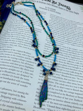 Load image into Gallery viewer, This celestial and galaxy goddess necklace features two strands of glass beading and a captivating Kyanite wired stone pendant. Its mixture of shimmering purples, blues, greens, and golds is truly striking and provides an alluring look like no other. Add this bold and beautiful jewelry piece to your collection today for a statement look that truly stands out. Necklace is 15” in length, can be adjusted to 18&quot;
