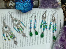 Load image into Gallery viewer, This Whimsical Blue Green Peacock Inspired Beaded Earrings set features bold chandelier style earrings with three long strands of glass bead. These show-stopping pieces boast a range of shimmering shades of blue, green, purple, and gold. A perfect addition to any fashionista&#39;s collection. Measurements: 3 1/2” in length
