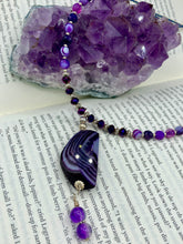 Load image into Gallery viewer, This double-stranded necklace is adorned with a large agate stone displaying a spectrum of purple shades, from light sheer to deep dark tones. The combination of purple agate and multi-colored glass beads makes this pendant a stunning addition to any summer look.  Measurements:  Necklace is 17” in length 
