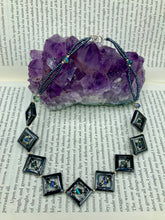 Load image into Gallery viewer, This two-strand necklace, crafted from aqua-blue and silver toned glass beads, is a stunning statement piece. The addition of faceted triangle-shaped glass beads tucked between hematite square beads adds an exquisite and unique flair. The necklace gracefully drapes around the neck, bringing an air of bold and elegant flair to any ensemble it complements. 15” in length, can be extended up to 17"
