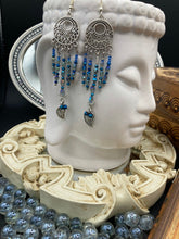 Load image into Gallery viewer, These intricate moroccan blue Inspired large chandelier earrings boast five strands of blue and iridescent glass beads of various hues, including silver and gold. Additionally, two small dark blue glass beads with a silver leaf add a touch of dimension and motion. The perfect addition to any Fairy Princess or whimsical aesthetic.  Measurements: 4” in length
