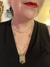 Load image into Gallery viewer, This stunning aqua blue and silver glass beaded necklace is a bold statement piece, composed of an adjustable necklace featuring blues, silver, and iridescent beads. Its shorter, collar style strand contains two-hole iridescent beads to keep its shape and adds a generous helping of iridescent teardrop glass beads for maximum sparkle. Its accompanying large, rectangular faceted pendant has a shimmering mix of gold, green, pink, and blue hues, and elegantly drapes across the neck.
