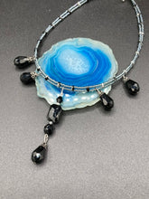 Load image into Gallery viewer, This adjustable collar-style necklace features silver and black glass beads in a combination of both teardrop and rectangular shapes, designed to create visual complexity and depth. The two strands are held together with two-hole silver and black beads, creating a stunningly bold and elegant draped collar that enhances any outfit.
