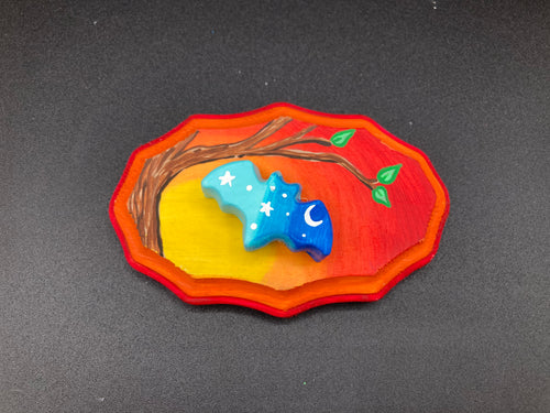 This unique Starry Night Mini Bat Wall Art Decor is hand sculpted and painted in vivid hues to offer an eye-catching decoration for your living space. The bat is painted in a gradient of light to dark blue, and is complemented by white stars and a crescent moon. The wood frame is painted in yellow, orange and red for a stunning sundown effect for a drastic contrast to the blue bat.