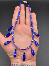 Load image into Gallery viewer, This Vibrant Royal Blue Glass Beaded Choker Necklace features two adjustable strands of deep blue beads with purple hues. The Bohemian style jewelry includes a mixture of rectangular-shaped blue, purple, and silver glass beads, which come together to create an eye-catching and elegant look. Perfect for any outfit, this draping necklace will add a vibrant and bold touch to your style.  Measurements:    Necklace is 14 3/4” in length, can be adjusted up to 16"
