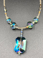 Load image into Gallery viewer, Make a bold statement with this shimmery aqua blue and gold tones glass beaded necklace. The large rectangular faceted shaped pendant creates a vivid contrast to the warm gold tones of the necklace, perfect for adding a rich pop of color to any Spring outfit. The draped design gives this piece an elegant, bohemian look. Measurements:    Necklace is 20” in length, 
