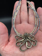 Load image into Gallery viewer, This stylish necklace features a silver plated metal octopus pendant and vibrant iridescent and silver-gray glass beads of various sizes. The Steampunk-inspired design provides a textured, patterned and voluminous look perfect for any dark goth or witchy aesthetic. Measurements:  Necklace measures 15 1/2” adjustable up to 17” in length
