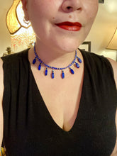 Load image into Gallery viewer, This Vibrant Royal Blue Glass Beaded Choker Necklace features two adjustable strands of deep blue beads with purple hues. The Bohemian style jewelry includes a mixture of rectangular-shaped blue, purple, and silver glass beads, which come together to create an eye-catching and elegant look. Perfect for any outfit, this draping necklace will add a vibrant and bold touch to your style.  Measurements:    Necklace is 14 3/4” in length, can be adjusted up to 16"
