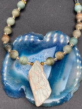 Load image into Gallery viewer, This exquisite necklace showcases earthy tones of mossy green ceramic beads, complemented by a gray toned howlite stone chip pendant. To add a sparkle, I interspersed gold-tone glass beads between each ceramic one. Two delicate strands feature small glass beads with hues of blue, gold, and purple. These are bridged by flower-shaped gold plated beads, which then unite with the round ceramic beads. This alluring earth-tone combination makes a stunning accessory. Necklace is 17” 
