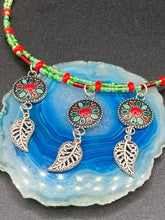 Load image into Gallery viewer, This adjustable necklace features an eye-catching Southwest-inspired design. Multi-hued glass beads, including bright green and vibrant red, are accompanied by dark red and green pendants with silver-plated feather charms. Ideal for chingona guerrera carbonas, la India princesses, warrior cosplay, and native-inspired looks.  Measurements:  Necklace is 15” adjustable up to 17" in length
