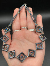 Load image into Gallery viewer, This two-strand necklace, crafted from aqua-blue and silver toned glass beads, is a stunning statement piece. The addition of faceted triangle-shaped glass beads tucked between hematite square beads adds an exquisite and unique flair. The necklace gracefully drapes around the neck, bringing an air of bold and elegant flair to any ensemble it complements. 15” in length, can be extended up to 17"
