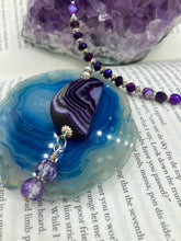 Load image into Gallery viewer, This double-stranded necklace is adorned with a large agate stone displaying a spectrum of purple shades, from light sheer to deep dark tones. The combination of purple agate and multi-colored glass beads makes this pendant a stunning addition to any summer look.  Measurements:  Necklace is 17” in length 
