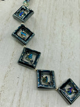 Load image into Gallery viewer, This two-strand necklace, crafted from aqua-blue and silver toned glass beads, is a stunning statement piece. The addition of faceted triangle-shaped glass beads tucked between hematite square beads adds an exquisite and unique flair. The necklace gracefully drapes around the neck, bringing an air of bold and elegant flair to any ensemble it complements. 15” in length, can be extended up to 17"
