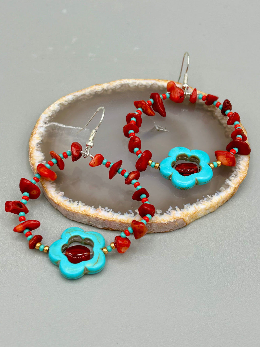 These Bamboo coral red stone chip earrings feature a subtle hoop design adorned with tiny turquoise, red, and gold glass beads. Completing the look is a turquoise flower pendant with a dark red glass bead in the center. Measurements: 2