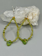 Load image into Gallery viewer, These natural peridot chips earrings feature a gold glass beading on their hoops, creating an eye-catching light green tone. A pressed glass leaf charm is also included, boasting an iridescent shimmer finish with subtle hints of gold, purple, blue, and pink.  Measurements: 2 1/2&quot; length
