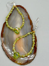 Load image into Gallery viewer, These natural peridot chips earrings feature a gold glass beading on their hoops, creating an eye-catching light green tone. A pressed glass leaf charm is also included, boasting an iridescent shimmer finish with subtle hints of gold, purple, blue, and pink.  Measurements: 2 1/2&quot; length
